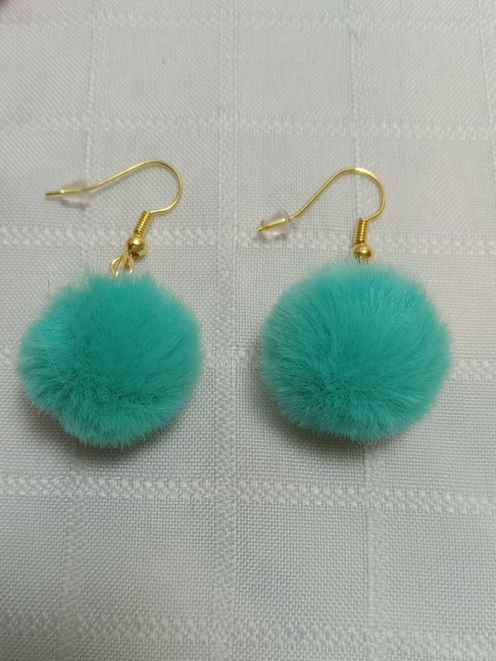 Handmade earrings with small pom-poms and gold-colored accent hooks